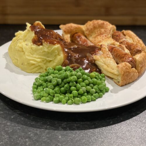 A plate of Toad in the Hole, mashed potatoes, onion gravy and peas