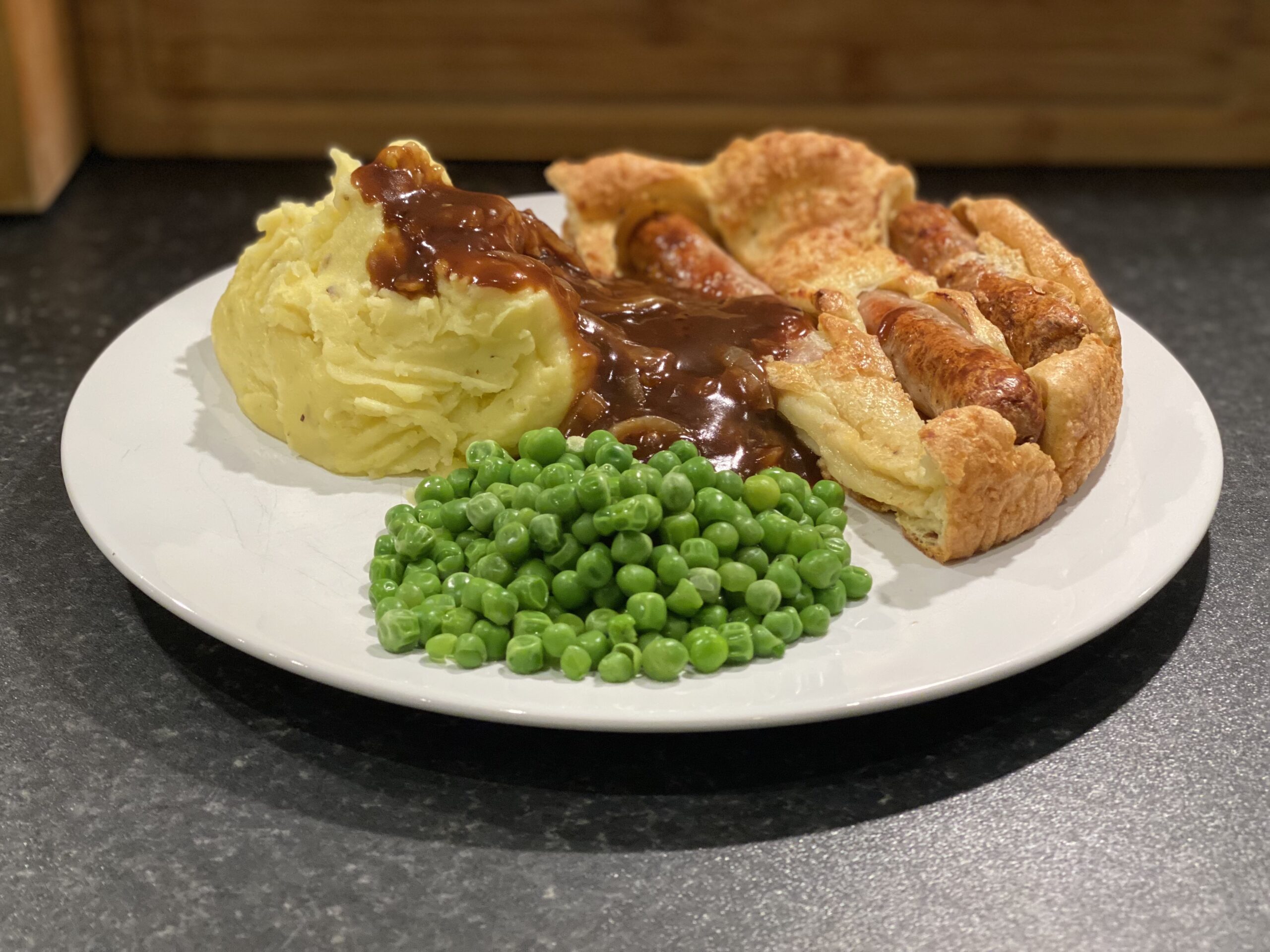 A plate of Toad in the Hole, mashed potatoes, onion gravy and peas