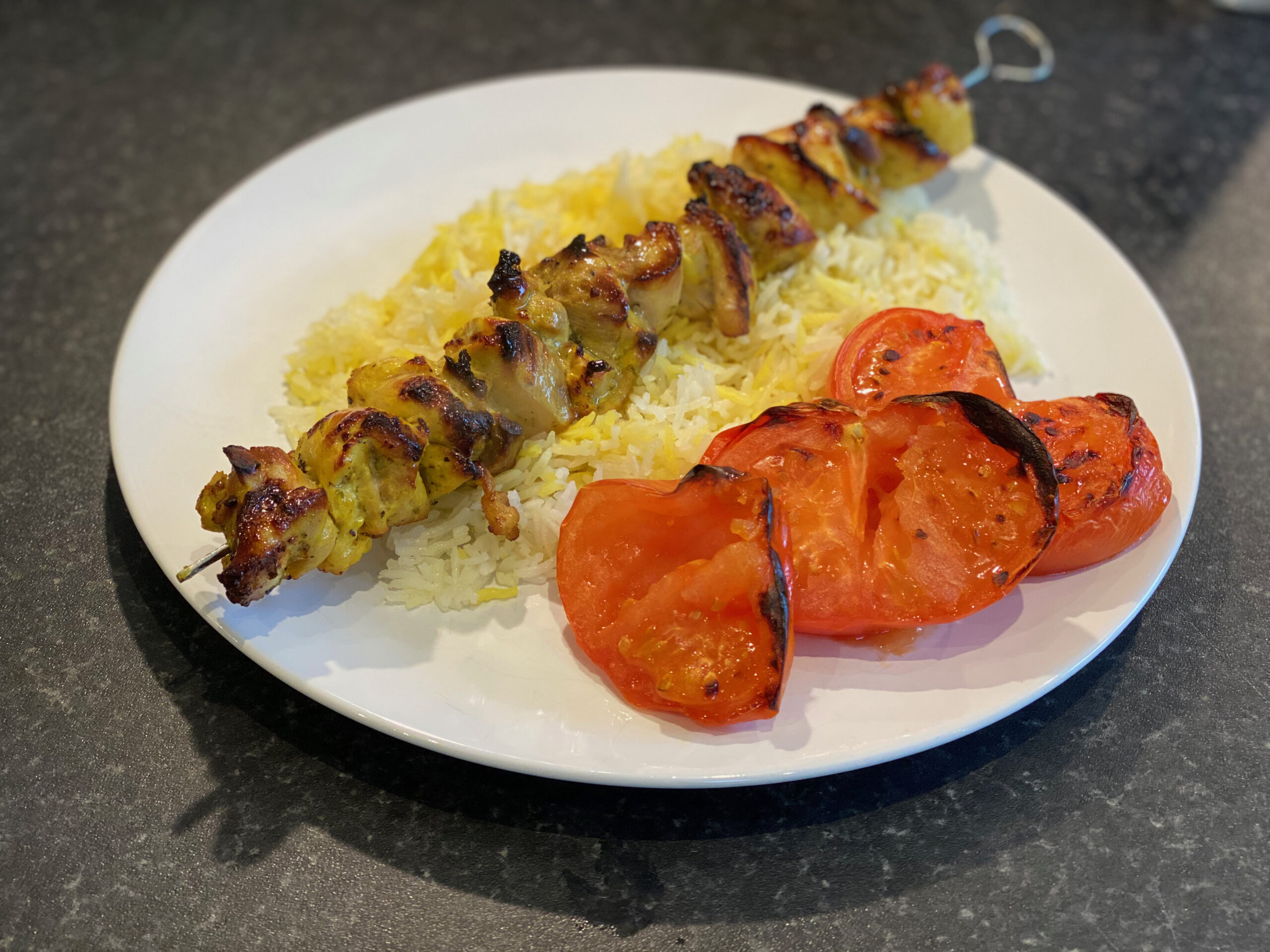 Chicken kebab on a bed of saffron rice and grilled tomato slices