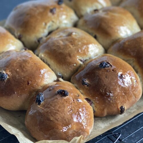 A dozen spiced fruited buns on a cooling rack